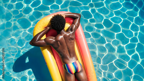 Gay man lying face down in swimming pool floating sunbathing in swimsuit with gay pride rainbow colors summer vacation at hotel. gay black man in summer sunbathing with athletic body photo