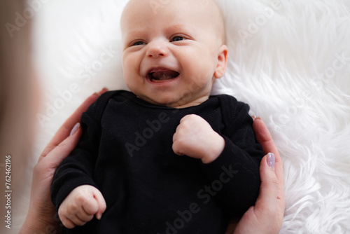 Ilittle baby dressed in a faithful bodysuit is lying on a white plush blunket. The two-month-old baby smiles to moms photo