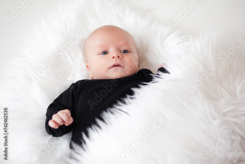 Ilittle baby dressed in a faithful bodysuit is lying on a white plush blunket photo