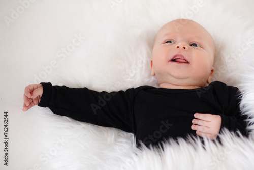 Ilittle baby dressed in a faithful bodysuit is lying on a white plush blunket photo