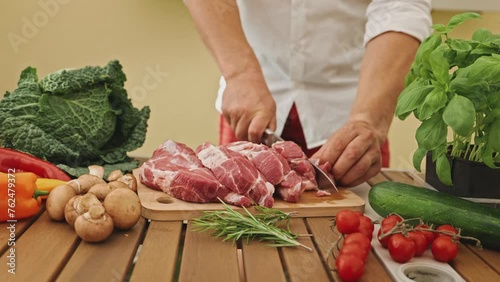 The hands of a chef with a knife in his hand cutting meat on the cutting board for preparing the recipe