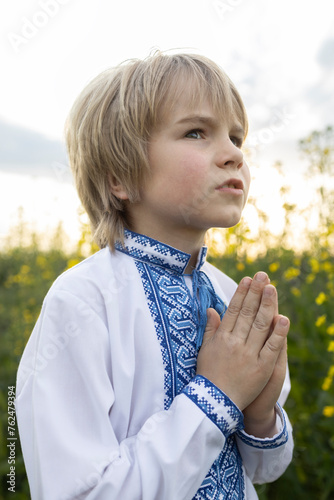 boy wearing a national Ukrainian embroidered shirt, folding his hands in prayer, turns to God. Children are against war. Ukrainian child asks for peace for his homeland