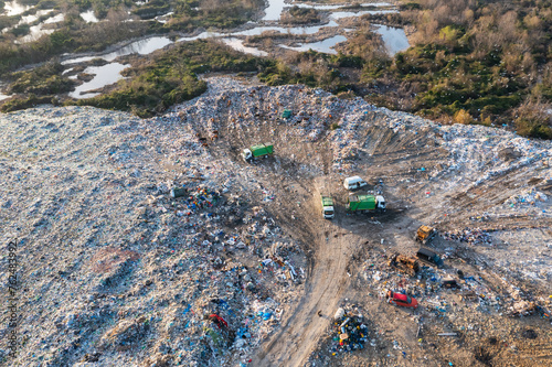 Aerial view of garbage pile in trash dump with dump track unload garbage at landfill. Biohazard for ecosystem and healthy environment concept. Environmental pollution and ecological disaster