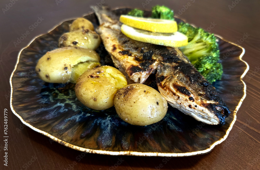 Golden roasted fish with potatoes, lemon and broccoli, served on wooden table. Overhead, horizontal - image Golden roasted fish with potatoes, lemon and broccoli, served on wooden table. Overhead, horizontal - image