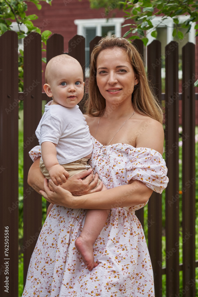 Fototapeta premium beautiful young mother in a summer dress and a one-year-old baby in the summer in nature among green trees