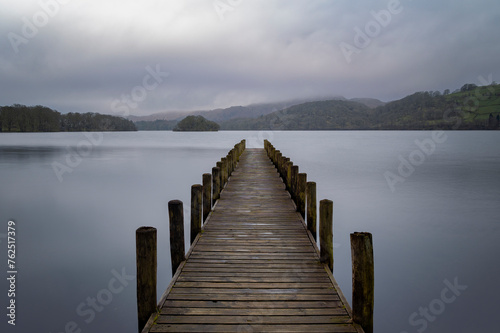 A wooden boat jetty reaching out over calm waters with mountains and islands on the horizon 