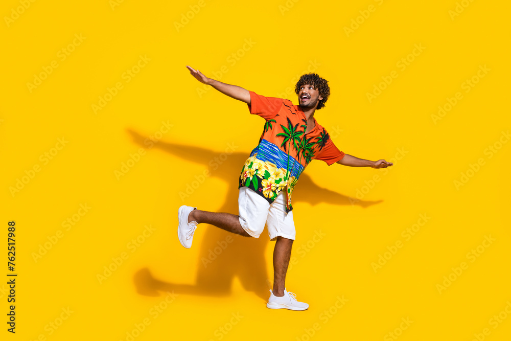 Full size photo of positive man dressed print shirt hold palms like wings look at promo empty space isolated on yellow color background