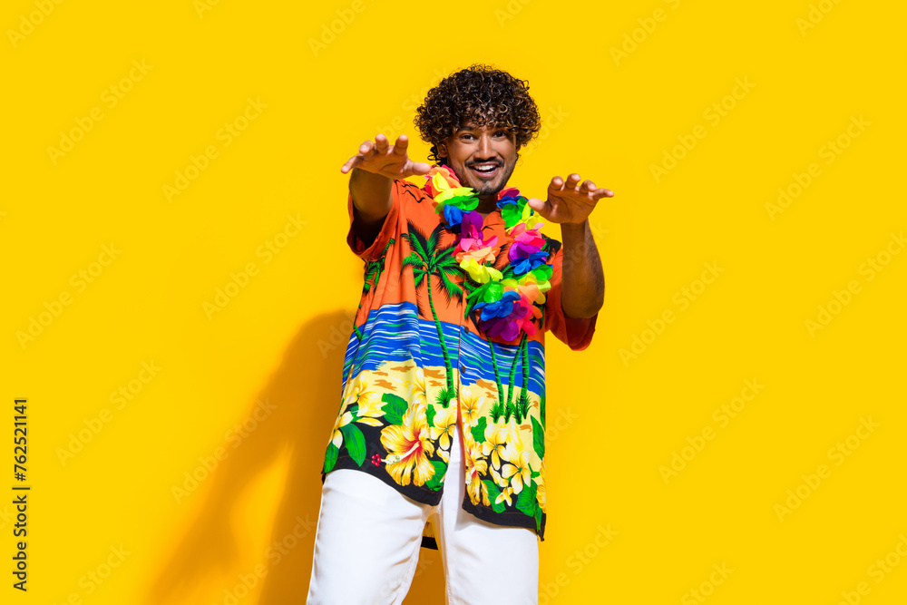 Photo of good mood man dressed print shirt flower necklace dancing stretching arms to you isolated on vivid yellow color background Photo of good mood man dressed print shirt flower necklace dancing stretching arms to you isolated on vivid yellow color background