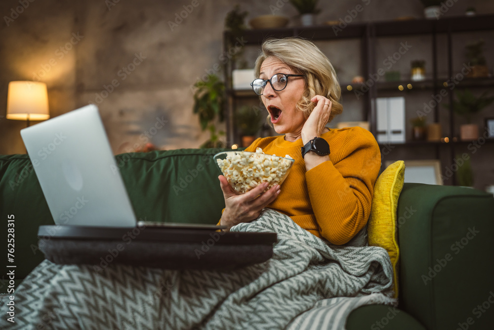 one mature blonde woman sit at home with watch movie video on laptop