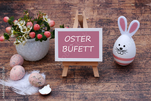 Der Text Osterbüfett ist auf eine Tafel geschrieben mit Ostereiern und Blumen geschmückt.	