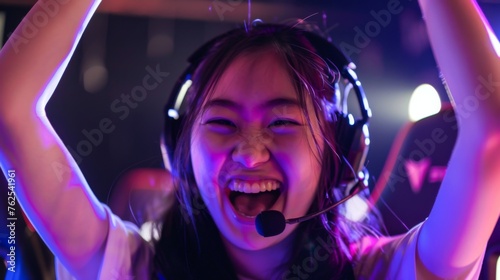 Asian woman wearing gaming headphones with a wide smile on her face celebrating her victory in an online video game