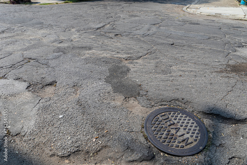 Intersection between streets in extremely derelict condition with patched and crumbling asphalt, old drain cover, creative copy space, horizontal aspect