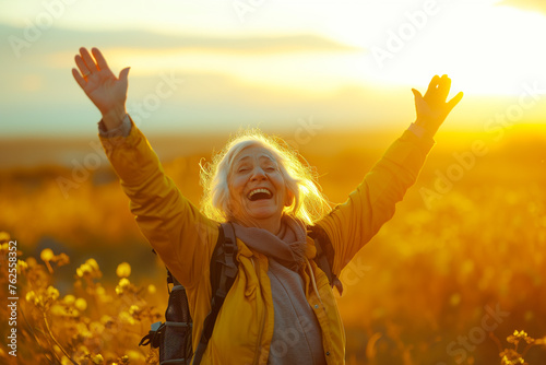 an older woman hiking at sunset with her arms in the air © AAA