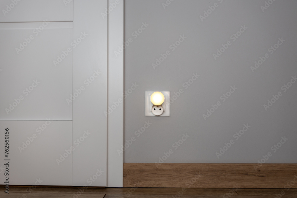 Obok drzwi znajduje się gniazdko z zasłonką emitującą światło, co symbolizuje połączenie konceptu elektryczności z ekonomicznymi zagadnieniami, zwłaszcza w kontekście wysokich rachunków za energię ele - obrazy, fototapety, plakaty 