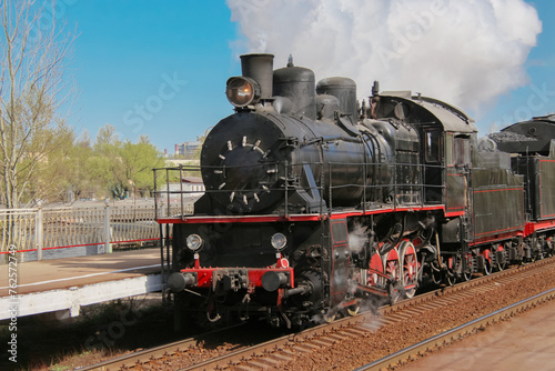 Tourist retro steam locomotive passing by the platform, releasing clouds of smoke from the chimney