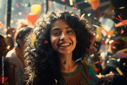 Woman with curly hair is smiling and surrounded by confetti. Scene is lively and festive  with people enjoying themselves and celebrating