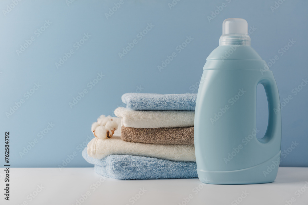 Blue container for liquid laundry detergent against the background of a stack of clean cotton towels - obrazy, fototapety, plakaty 
