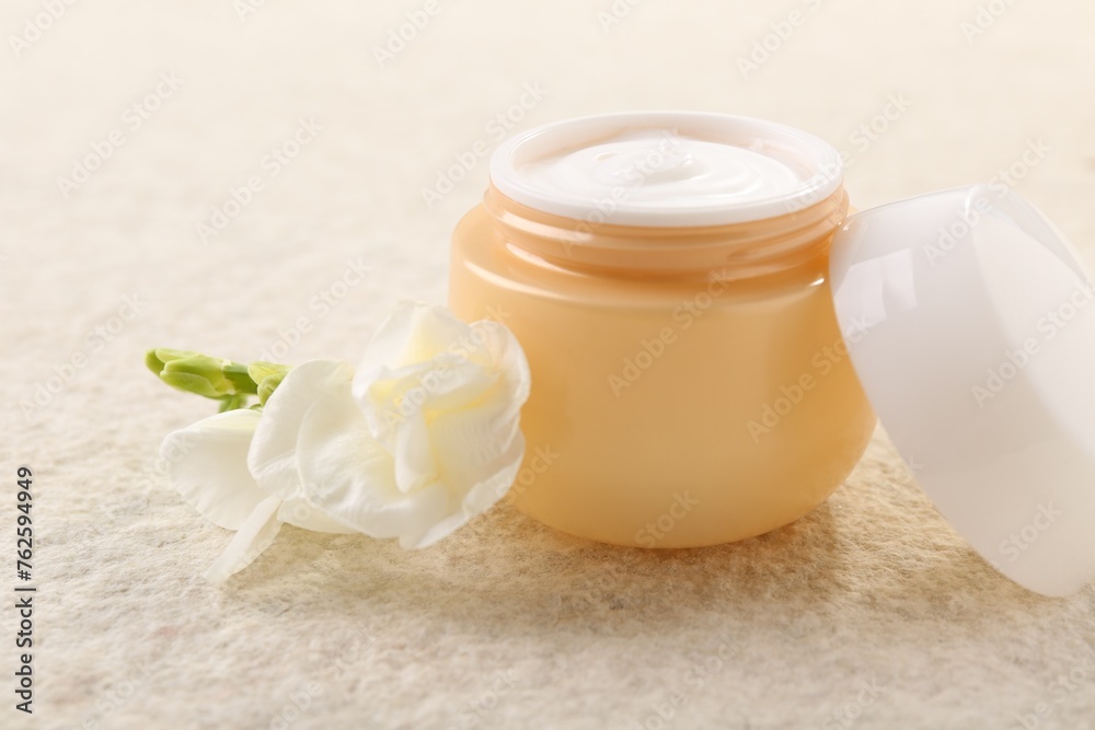 Body care. Moisturizing cream in open jar and flower on light textured table, closeup Body care. Moisturizing cream in open jar and flower on light textured table, closeup