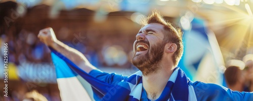 Happy Scottish male supporter with Scottish flag, Scottish male fan at a sports event such as football or rugby match, blurry stadium background, copy space © Pixelmagic