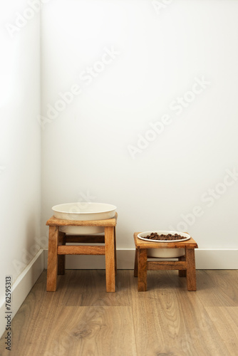 Dog feeding bowls on wooden stand. Water and biscuit pet food modern home corner, vertical © Olha Kozachenko