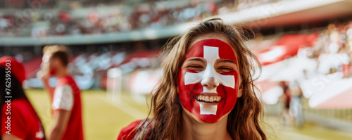 Happy Swiss female supporter with face painted in Swiss flag displays a white cross in the centre of a square red field, Swiss male fan at a sports event such as football or rugby match photo