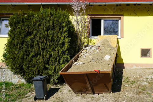 A large metal container full of construction debris near the window of a house under repair