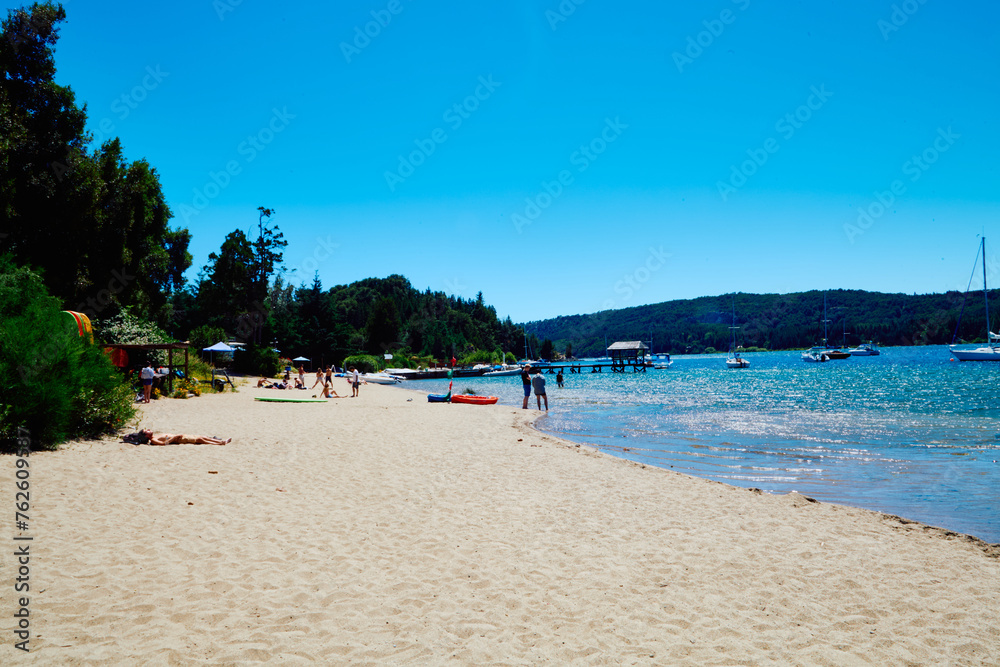 sandy beach on the shore of a blue lake with a pier for boats and yachts