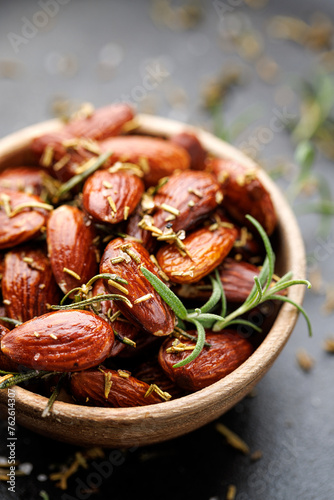 Close up of roasted almonds with rosemary in a wooden bowl on a grey background