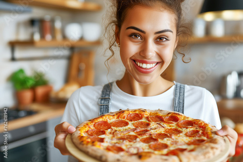 Smiling young woman holding pizza pepperoni in the kitchen
