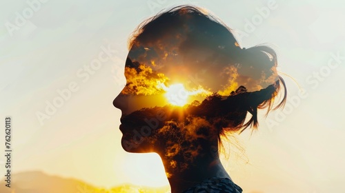 A womans face is silhouetted against the bright golden sun shining from behind her. The sun rays create a halo effect around her head.
