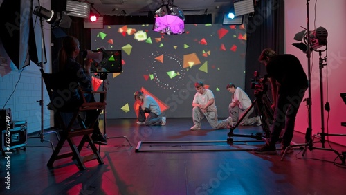 Backstage video shoot. Two girls and a guy dancing against a big LED screen with bright backgrounds.