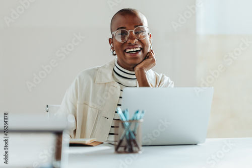 Happy young woman working on a laptop in bright office, expressing success and positivity
