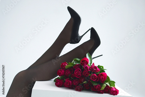 legs of a young woman in stockings and elegant shoes on a white background in a composition with red flowers