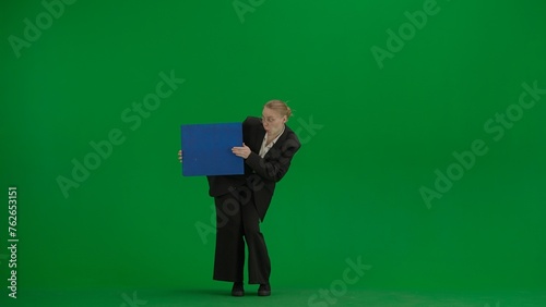 Portrait of female in suit on chroma key green screen. Blonde business woman in formal outfit holding advertisement board, dancing smiling face.
