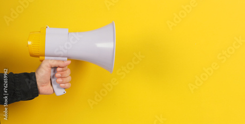 Hand is hold megaphone and wear black shirt on yellow background.