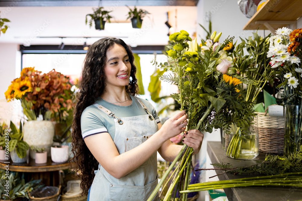 A young Latina dressed in an apron works inside a flower shop.Colombian woman making a bouquet of flowers for a customer.Concept of working woman.