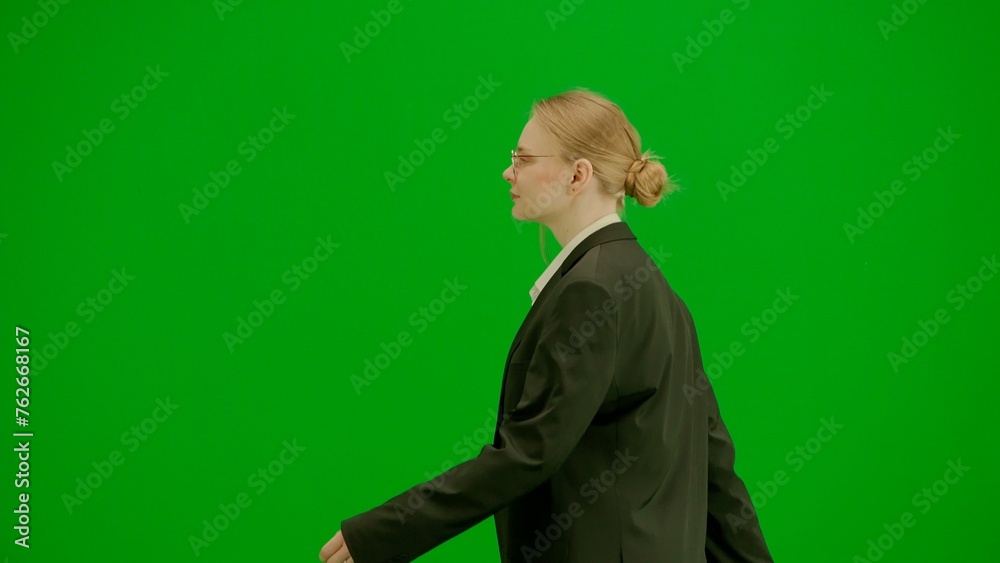 Portrait of female in suit on chroma key green screen. Blonde business woman in formal outfit walking with confident focused face expression. Side view. Portrait of female in suit on chroma key green screen. Blonde business woman in formal outfit walking with confident focused face expression. Side view.