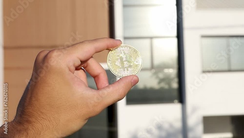 Pessoa segurando moeda de bitcoin, casa de fundo photo