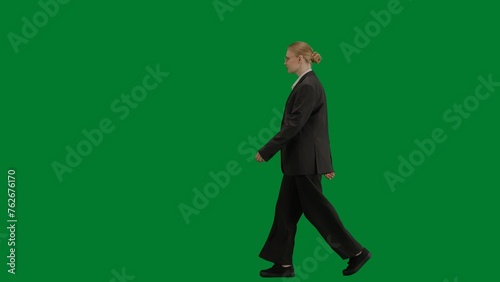 Portrait of female in suit on chroma key green screen. Blonde business woman in formal outfit walking with confident focused face expression. © kinomaster