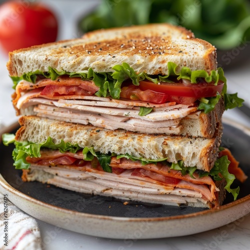 A sandwich with lettuce, tomato, and ham is cut in half and placed on a plate