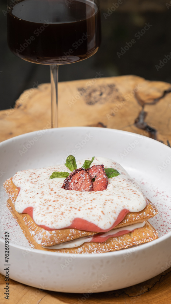 Belgian waffles with strawberry confit and cream sauce and glass on wooden table in cafe