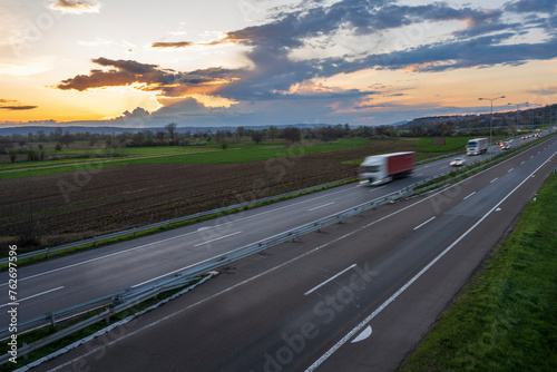 Truck drive at high speed on the highway through the rural landscape. Fast blurred highway driving. A scene of speeding on the highway. Beautiful sunset in the background.
