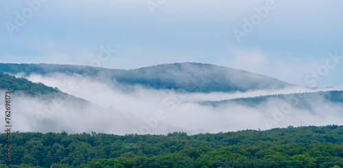 Wooded mountains, fog and vapor, blue sky, landscape landscape.
