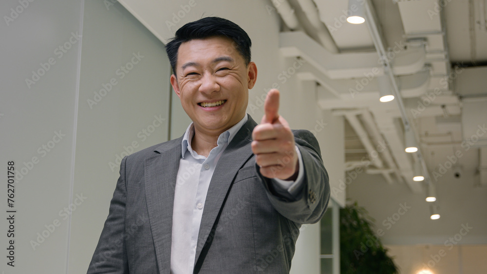 Satisfied Asian man happy middle-aged businessman korean chinese japanese ethnic male employer entrepreneur CEO executive showing thumb up like gesture business success achievement in office hallway
