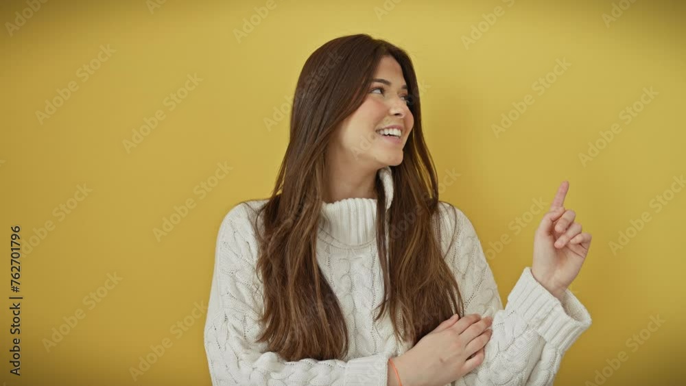 Cheerful young hispanic woman wearing a cozy sweater, confidently points to the side and beams at camera, background bathed in isolated yellow! Cheerful young hispanic woman wearing a cozy sweater, confidently points to the side and beams at camera, background bathed in isolated yellow!