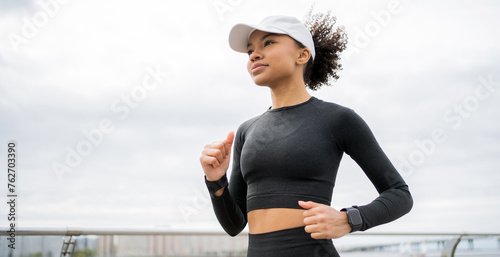Determined woman in sportswear jogging with focus  wearing a fitness tracker and cap.