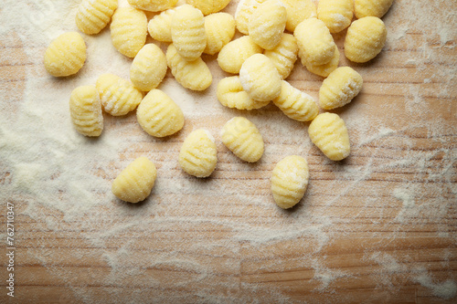 Potato gnocchi with durum wheat flour on wooden pastry board, top view, space for text, close-up.