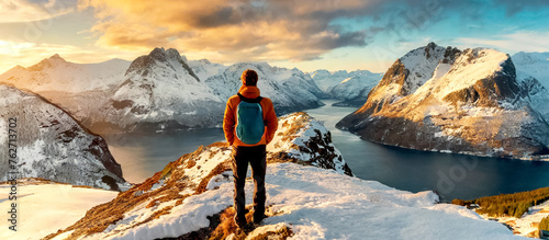 Mann steht auf Berggipfel mit Blick über eine Landschaft mit Bergen und Fjorden  photo