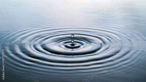 A single, pristine water drop falls into a calm pool, creating a series of perfectly symmetrical circular waves that ripple outward.