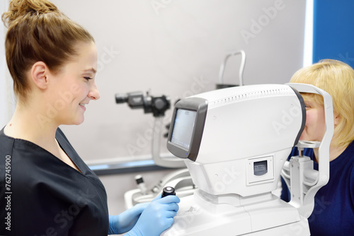 Examining of fundus of mature woman by female ophthalmologist using retinal scanner. Patient during visit to optometrist for microscopic analysis of eyelids, sclera, conjunctiva, iris, lens, cornea.